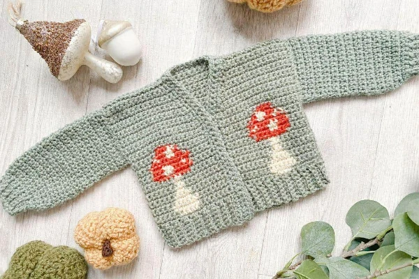 Crochet newborn cardigan with mushroom motifs.