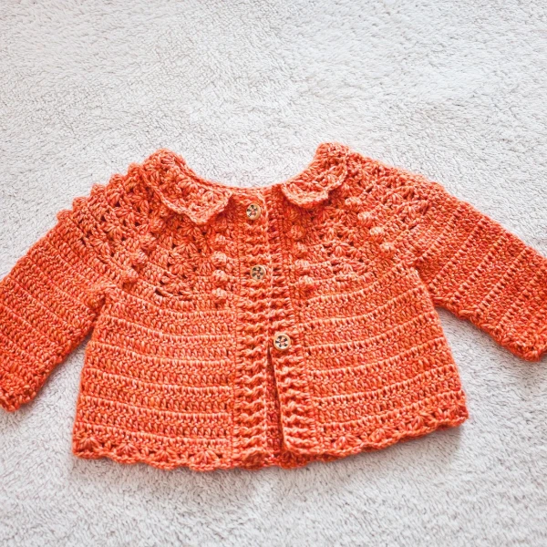 Crochet newborn cardigan with a collar and lacy shell stitch edging.