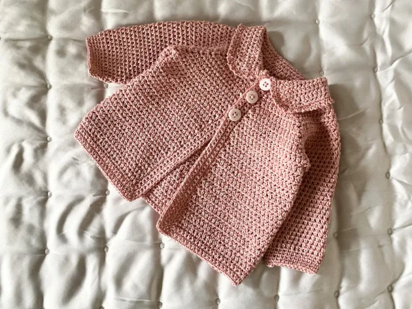 A pink crochet baby cardigan with a peter pan style collar.