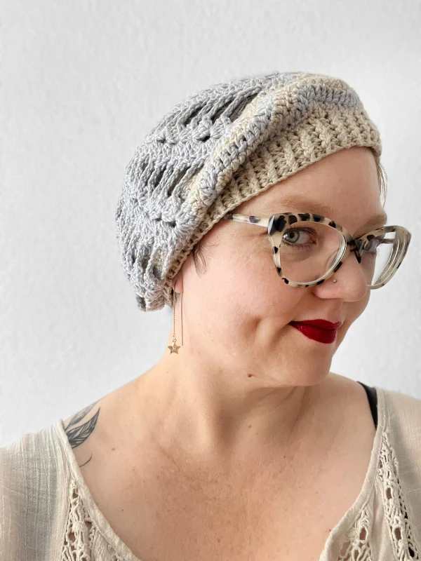 A grey crochet beret with an open, lacy look stitch pattern.