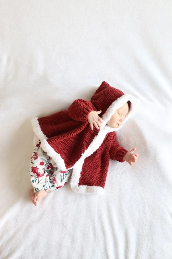 A newborn baby wearing a fur-trimmed crochet Christmas jacket.