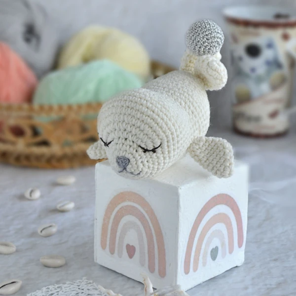 A baby seal crochet toy balancing on a block,