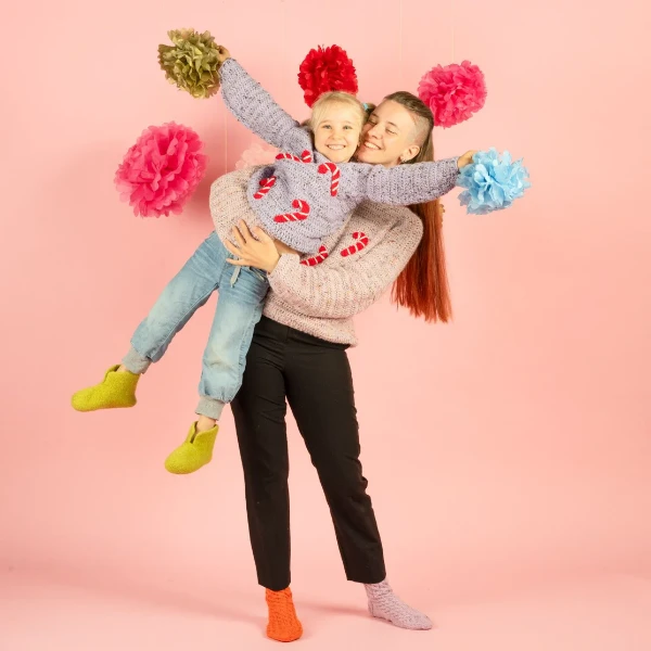 A mother and child wearing matching crochet Christmas sweaters featuring candy cane motifs.