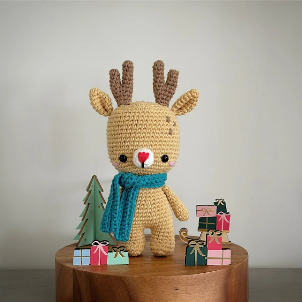 A crochet reindeer doll dressed in a scarf.