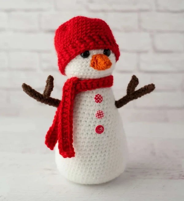 A crochet snowman dressed in a red scarf and hat.