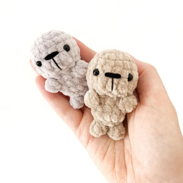 Two mini crochet seal toys held in the palm of a hand.
