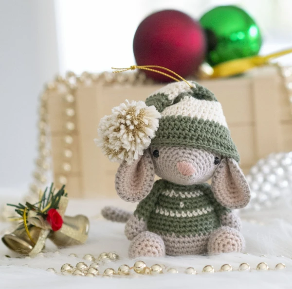 A crochet mouse amigurumi wearing a sweater and Christmas hat.