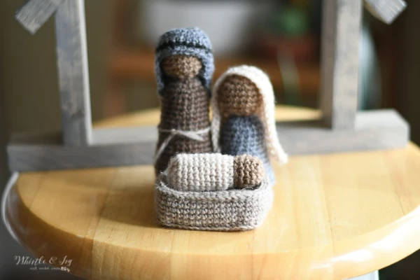 A crochet nativity set with Joseph, Mary, and Baby Jesus in a manger.