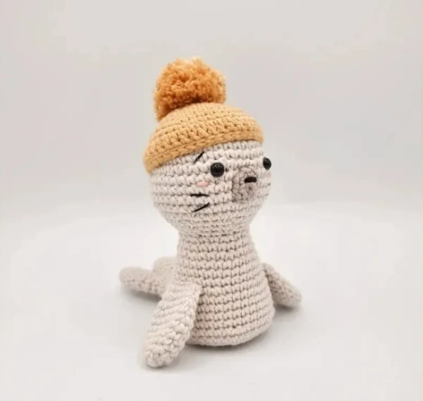 A crochet seal toy waearing a yellow beanie.