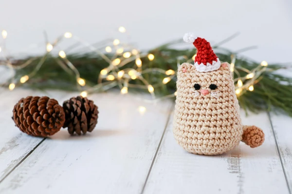 A miniature crochet cat wearing a Santa hat.