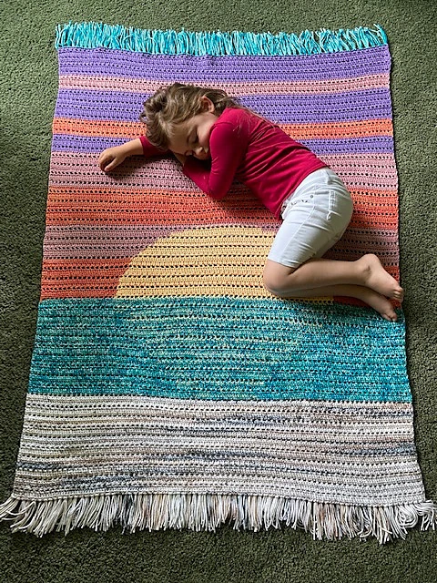 A child laying on a sunset-themed crochet blanket.