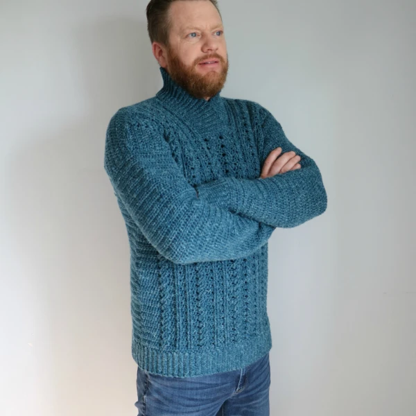 A man wearing a turquoise blue crochet sweater with cable stitch design.