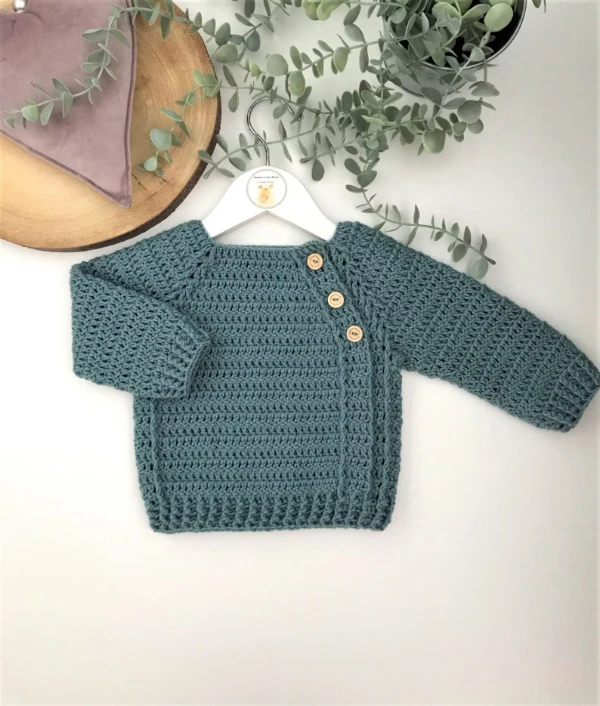 A blue crochet baby sweater with buttons at neck.