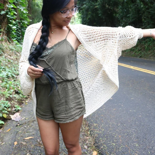 A woman wearing a mesh stitch crochet cocoon shrug over a khaki jumpsuit.