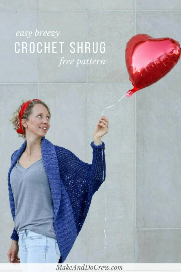 A woman wearing a bright blue oversized crochet shrug over jeans and a tee.