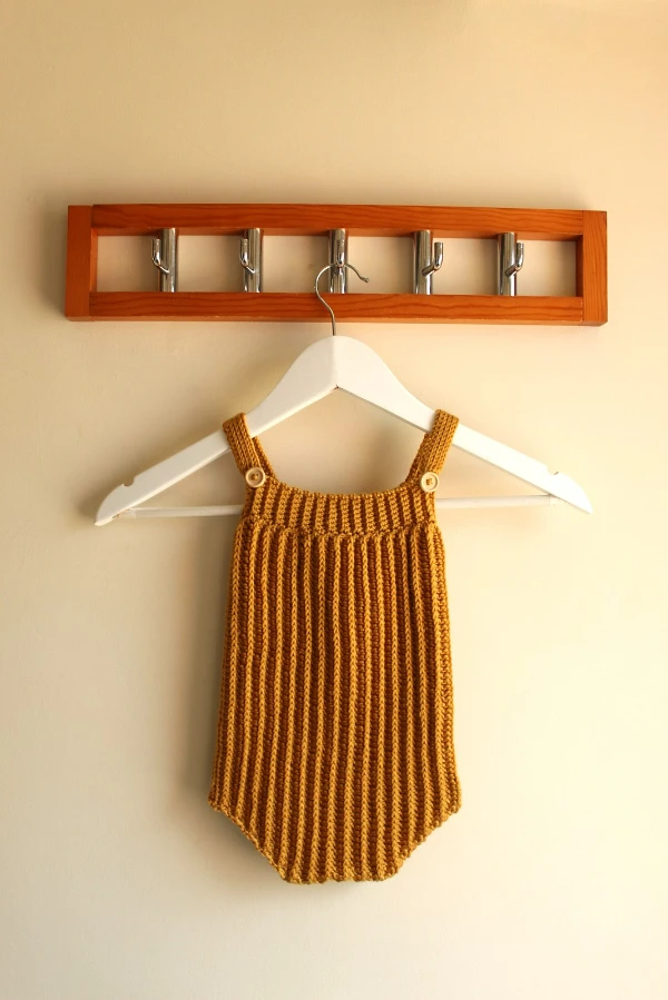 A mustard coloured sleeveless crochet baby romper on a wooden hanger.