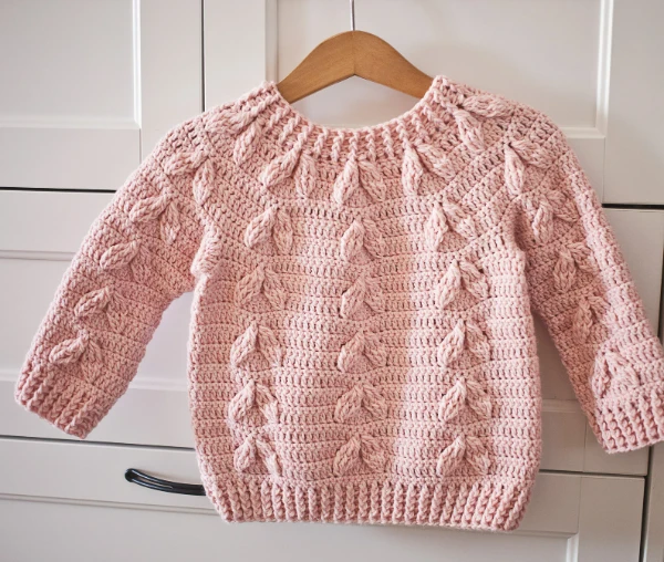 A pink crochet baby sweater with leaf-shaped motifs.