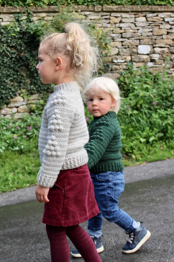 Two young children wearing matching crochet sweaters.