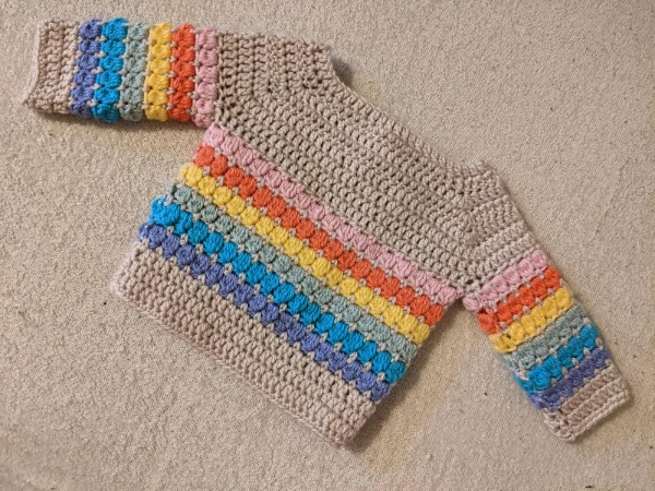 A cluster stitch crochet baby sweater with rainbow stripes.