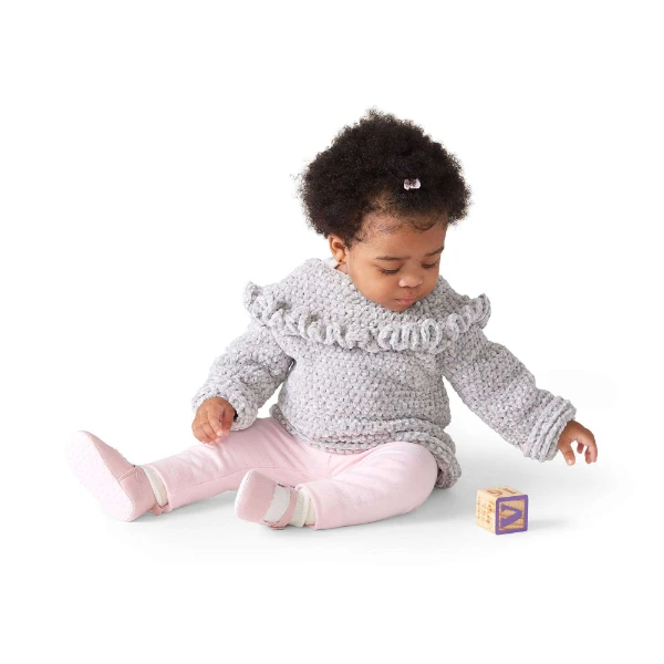 A baby girl wearing a ruffled crochet sweater.