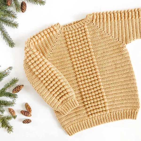 A butter yeloow crochet baby sweater with bobble stitch detail.