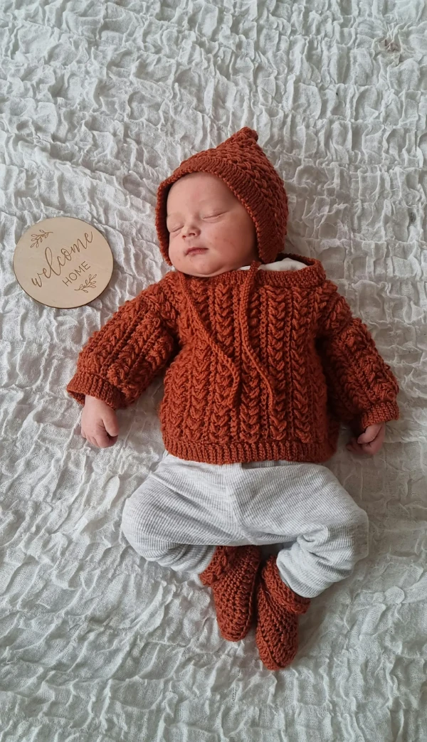A newborn baby wearing a crochet sweater with matching booties and bonnet.