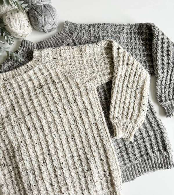 Flat lay image of two men's crochet sweaters in shades of grey.
