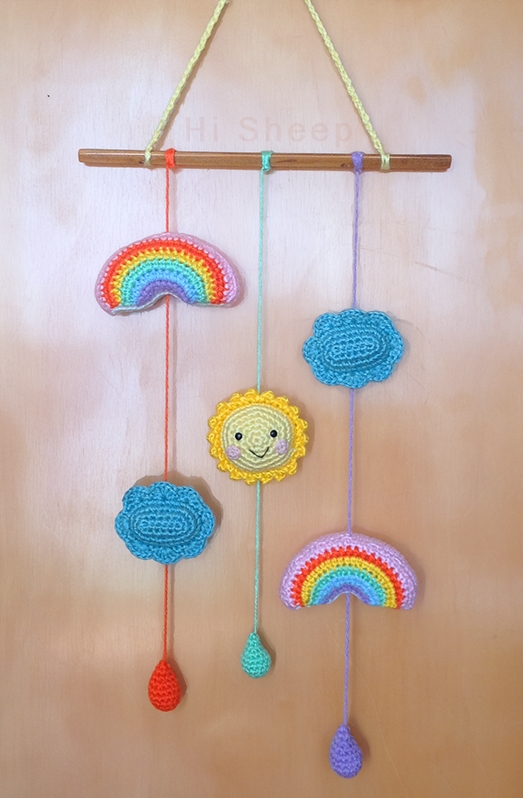 A brightly coloured crib mobile faturing a sun, clouds, and rainbows.