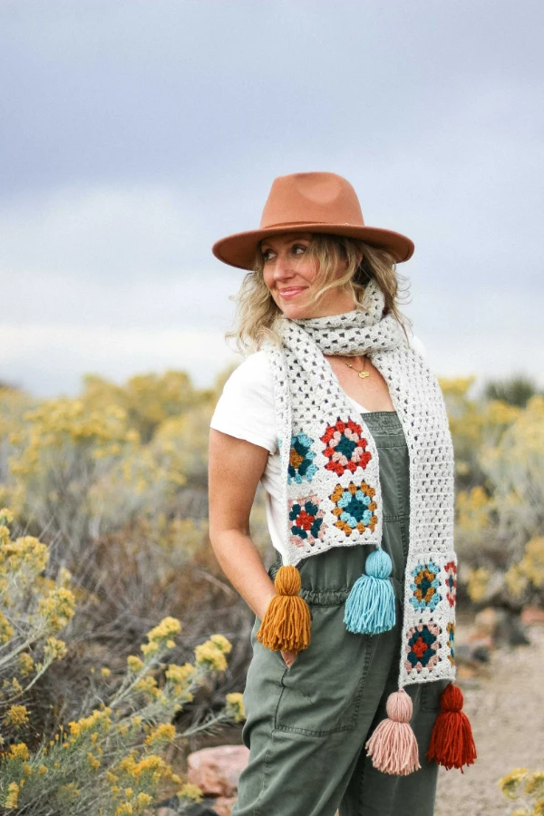 A woman wearing a colourful granny square scarf with tassels.