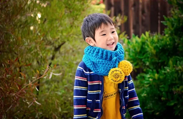 A boy wearing a chunky crochet cowl with pompoms.