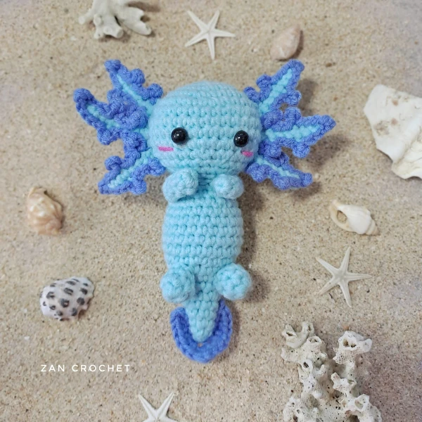 A flat lay image of a blue crochet axolotl toy.