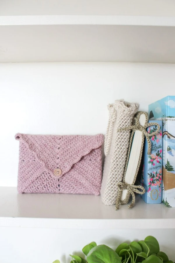 A pinck, envelope-style crochet book cover on a shelf.