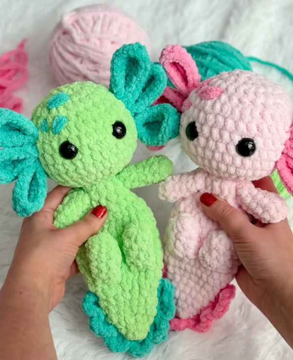 Two soft crochet axolotl plushies - one green and one pink.