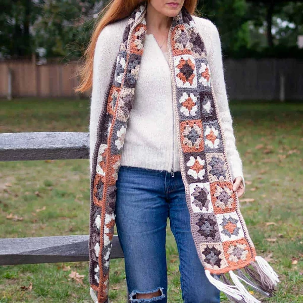 A woman wearing a long granny square crochet scarf.