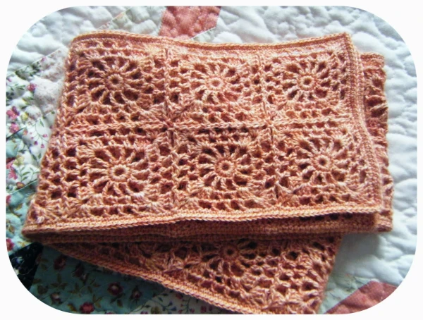 A peach coloured lacy granny square crochet scarf.