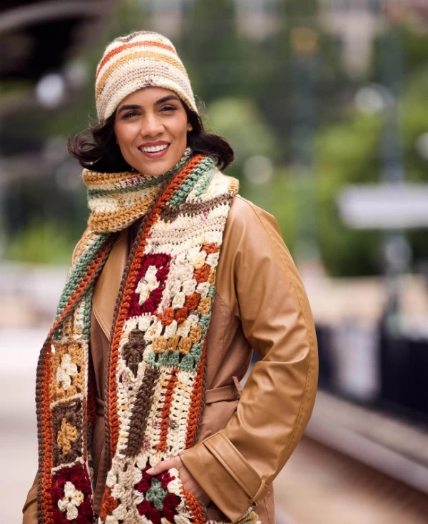 A woman wearing a multicoloured crochet granny square scarf and hat.