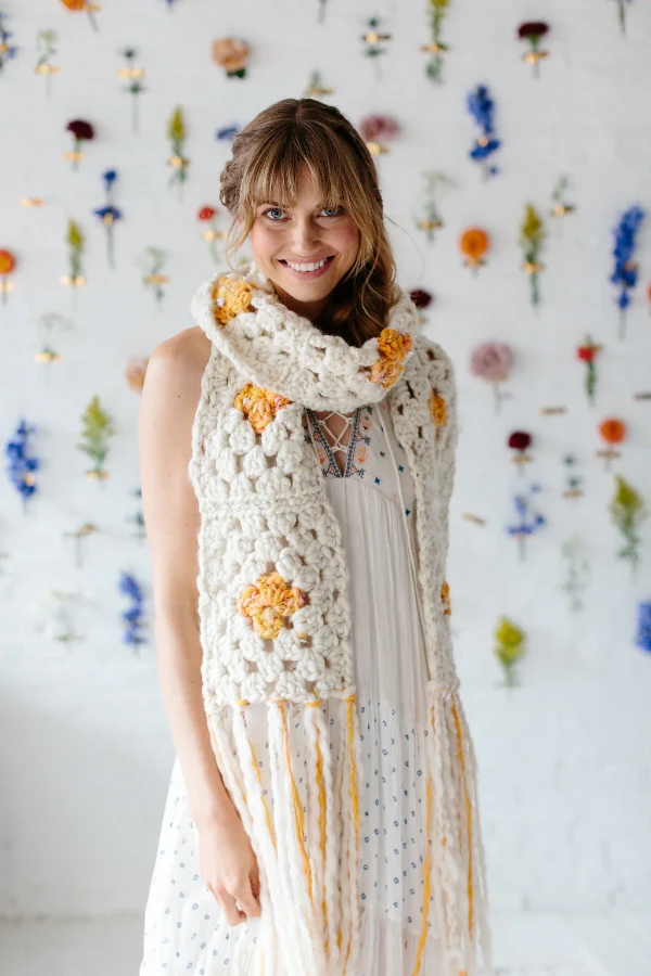 A woman wearing a yellow and white granny square scarf crocheted in super bulky weight yarn.