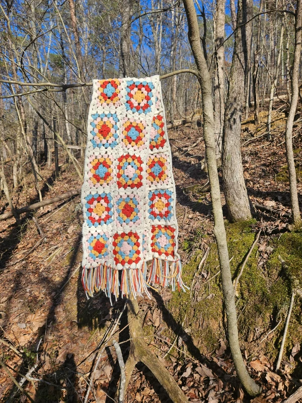 A colourful granny square scarf with tasseled edges.