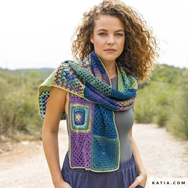 A woman wearing a crocheted granny square scarf made with graident yarn.