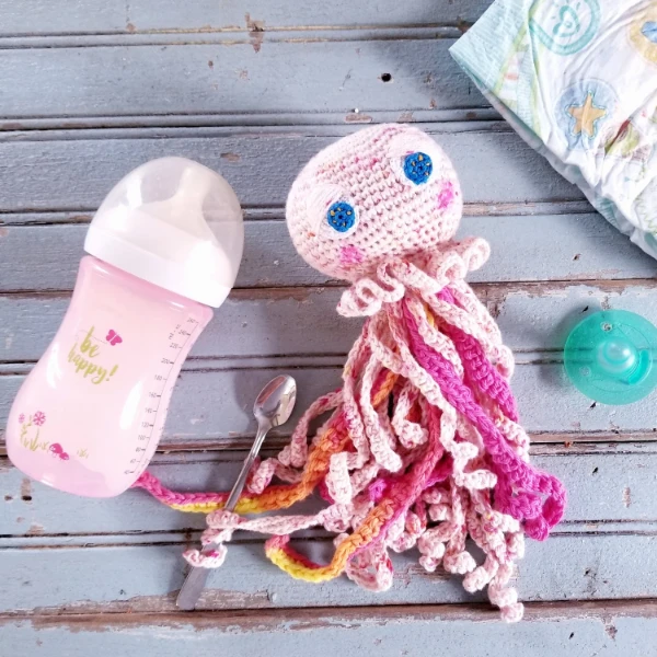 A pink crochet jellyfish with big embroidered eyes.
