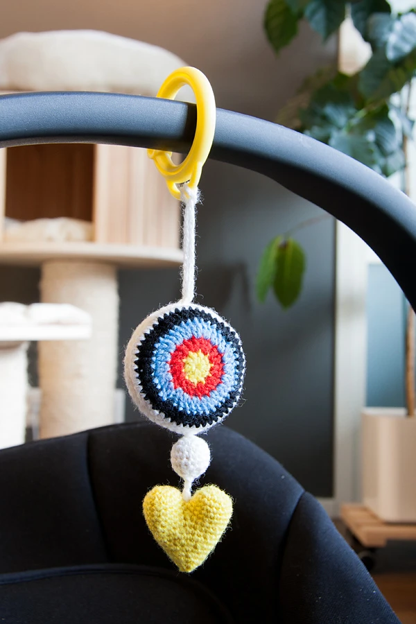 A crochet bullseye toy hanging from a stroller.