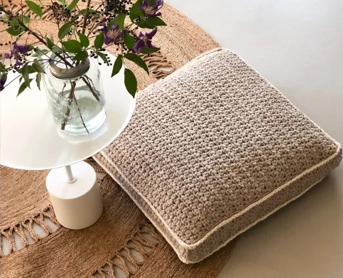 A crochet floor cushion next to a table and plant.