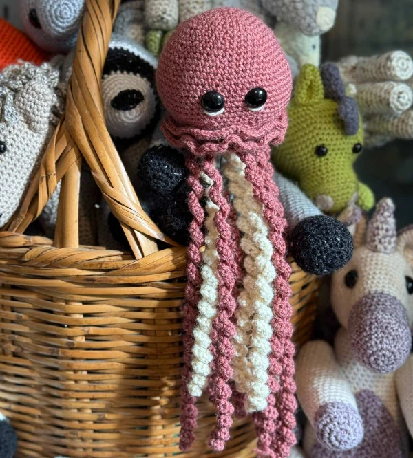A pink and white crochet jellyfish toy with extra long tentacles.