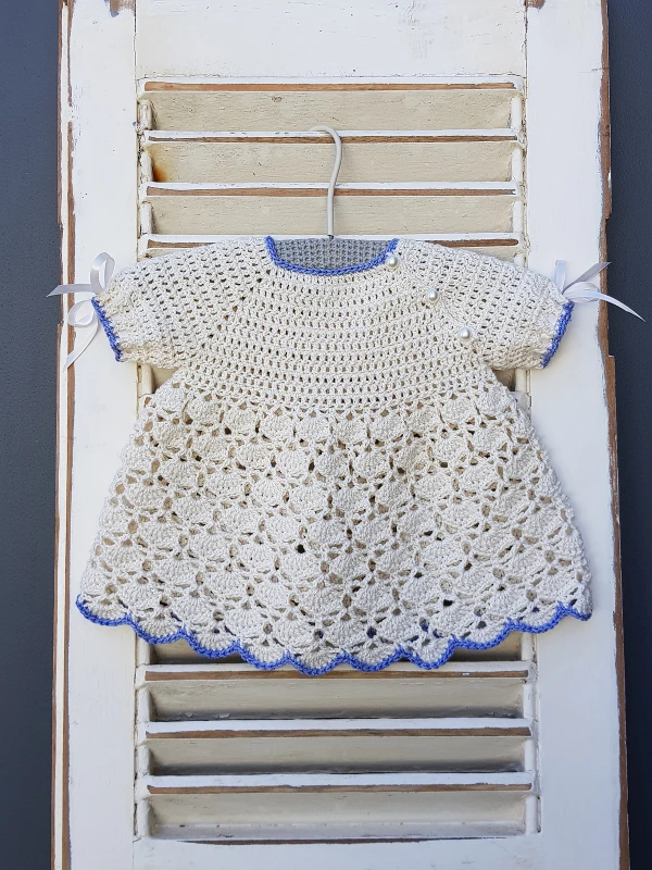 A white crochet baby dress with blue trim.