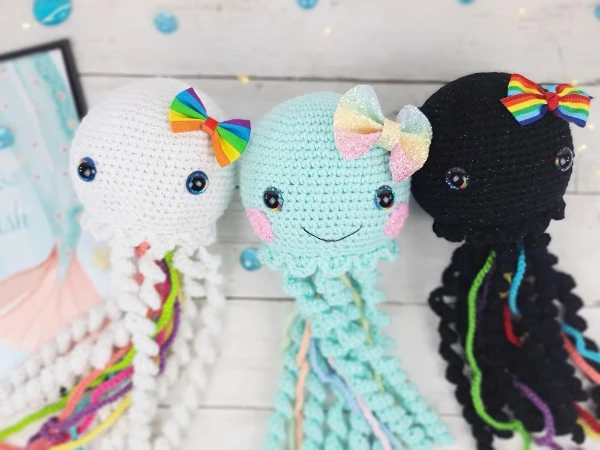 Three different coloured crochet jellyfish toys with rainbow bows.
