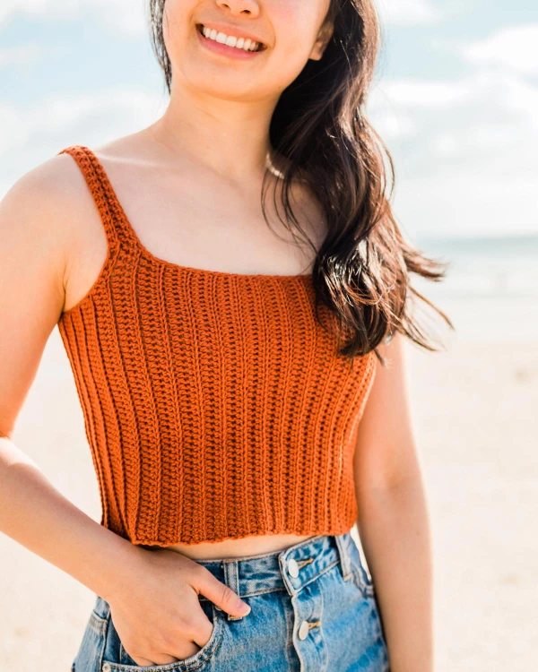Woman wearing a rust coloured crochet ribbed tank top.