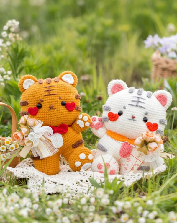 Two amigurumi tiger toys sitting on a picnic rug.