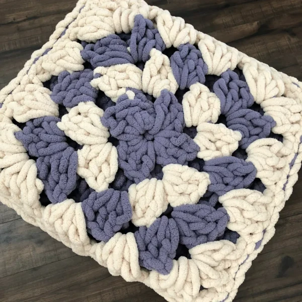 A grey and white giant granny square crochet floor pillow.