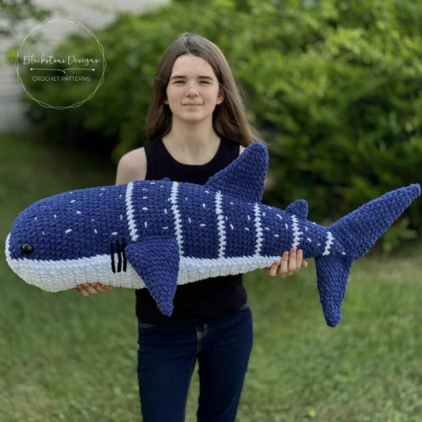 A woman holding a gian crochet whale shark plush toy.