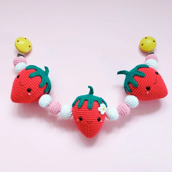 A crochet stroller toy with a plush strawberry theme.